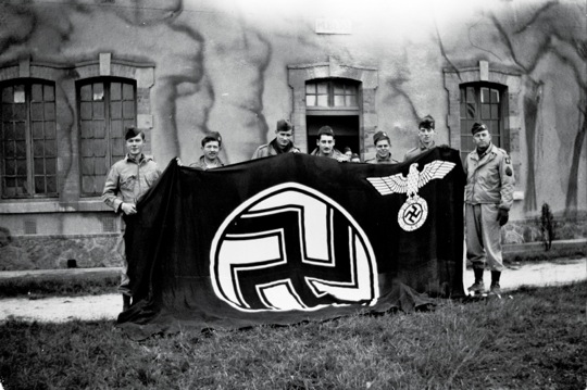 Tech/5 Brad Hinchliff (third from left) posing with captured German flag from the September 17th 1944 Holland combat jump.